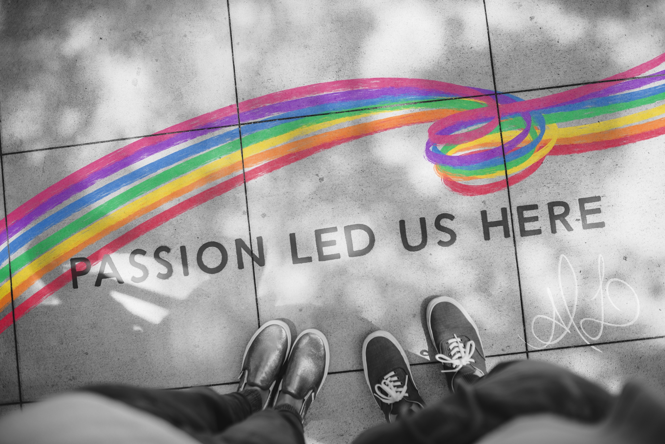 A sidewalk covered in swirling rainbow chalk art and block text that says Passion Lead Us Here