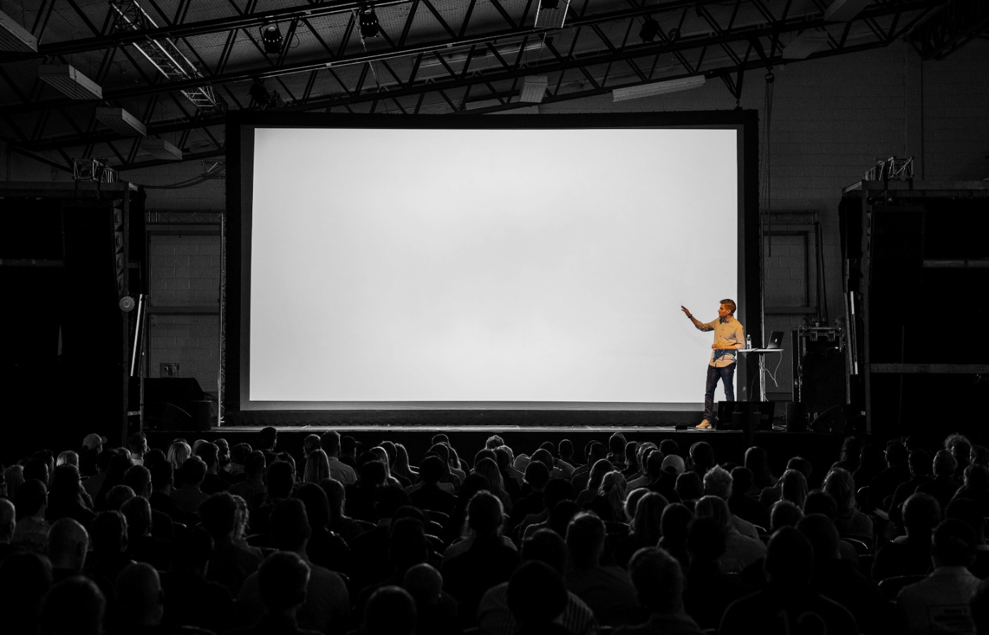 A man standing on a stage in front of a large audience, with a blank screen behind him