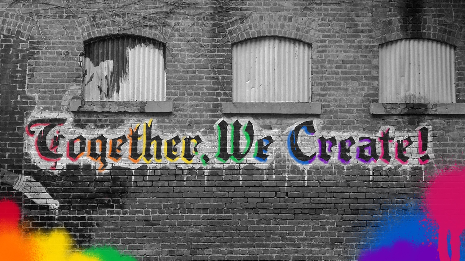 An industrial brick wall with rainbow graffiti that says together we create