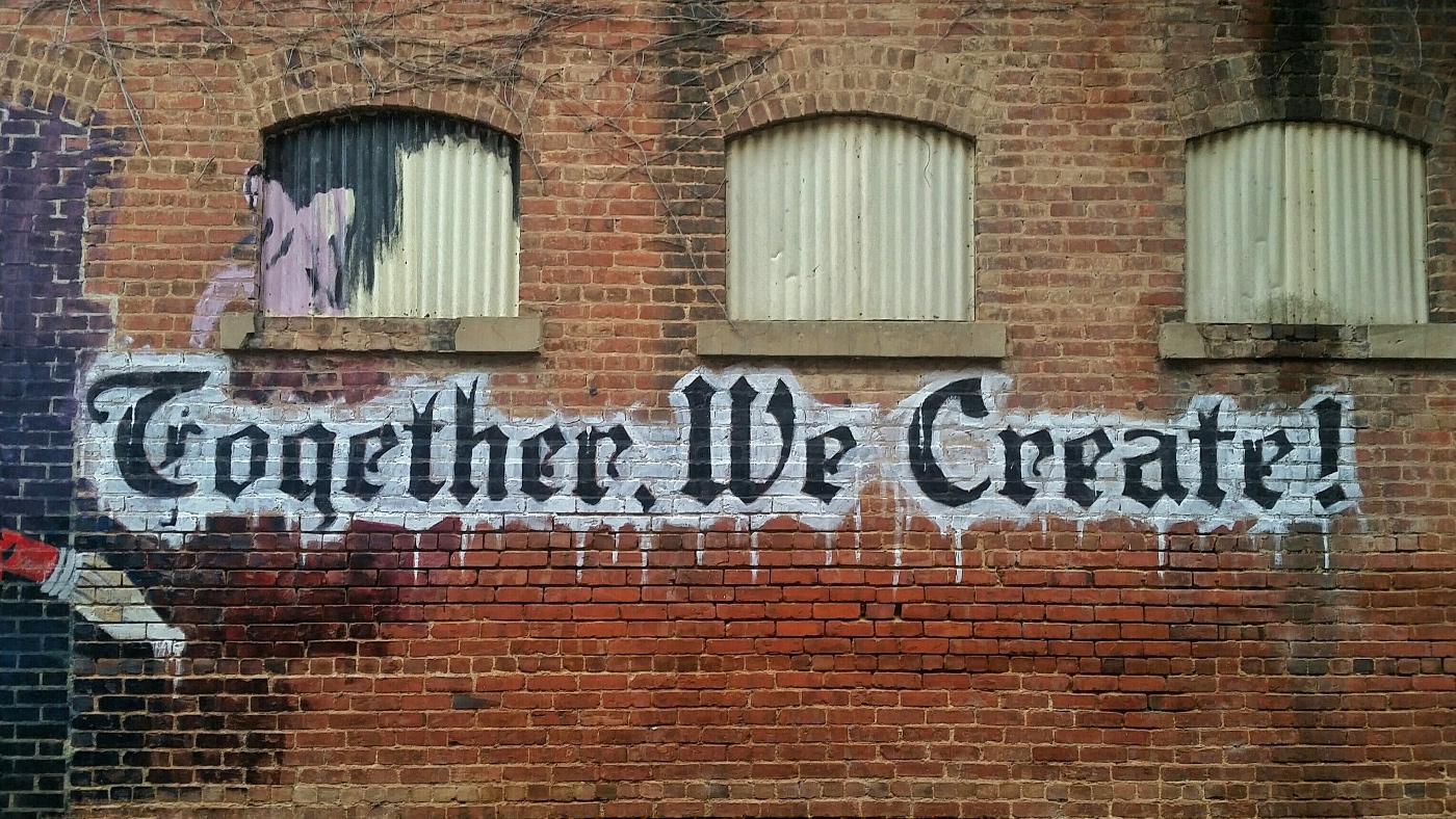 A brick wall with the words Together We Create spray-painted on