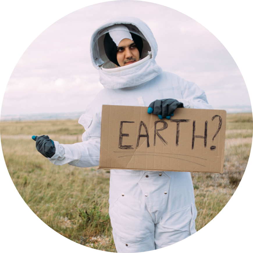 An adult wearing an astronaut suit, his thumb sticking out trying to hitch a lift, and holding a cardboard sign that says, "Earth?"
