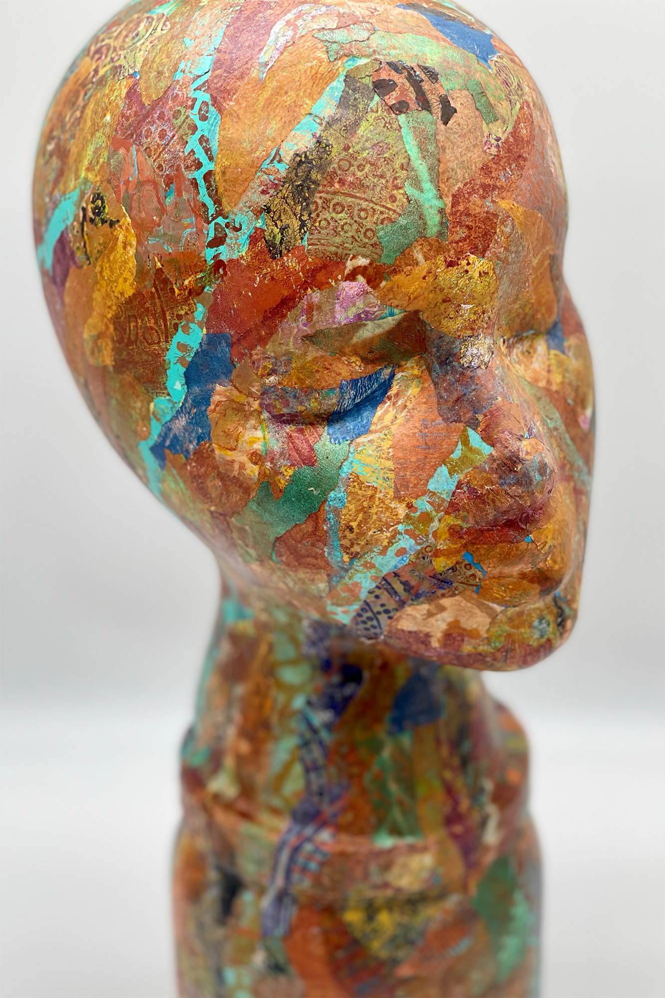 A photograph of an original sculpture by A.H. Lawver, entitled "Liv". It's a bald, minimalist head, splattered with a wide variety of color monoprints.