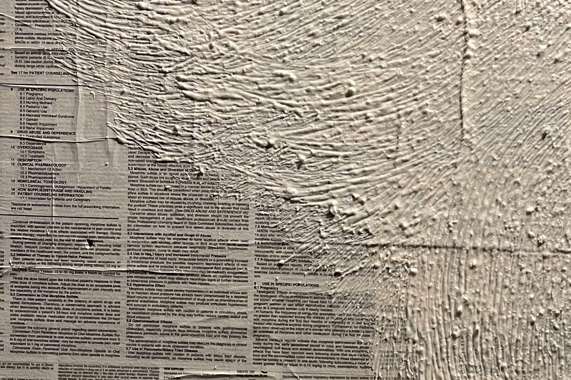 A close up of part of a mixed media painting created by Heather Lawver titled "Icarus Oath", created using crushed up Tylenol mixed in gesso, atop a canvas covered in collaged narcotic drug information insert papers.