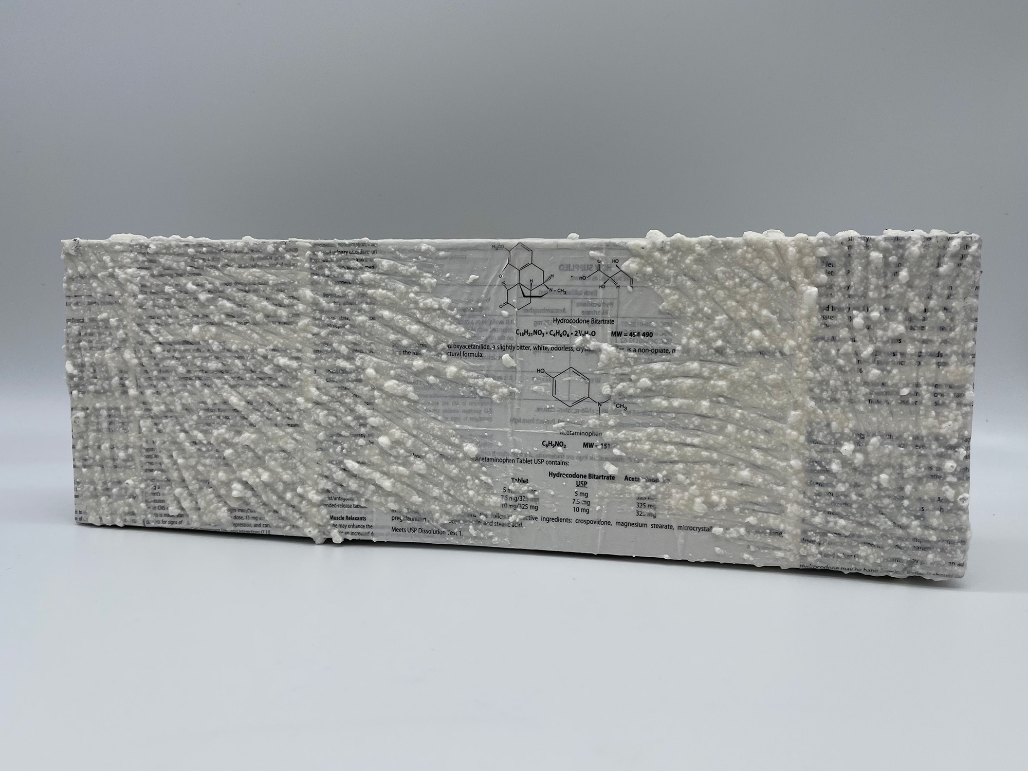 An original mixed media painting by H.M.A. Lawver, 3/5. Created using crushed tylenol mixed with gesso & acrylic, painted atop a canvas covered in collaged narcotic drug information inserts. 