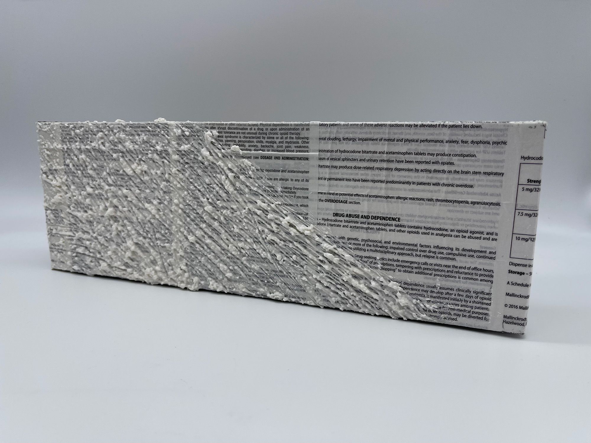 An original mixed media painting by H.M.A. Lawver, 5/5. Created using crushed tylenol mixed with gesso & acrylic, painted atop a canvas covered in collaged narcotic drug information inserts. 