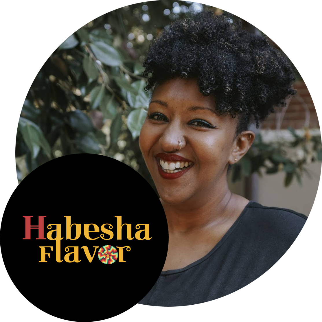Logo & promotional image from Habesha Flavor. In the photo, you can see Founder, Chef Micknai Arefaine, smiling at the viewer, standing in front of a leafy green background. Her fabulously curly dark hair is in a joyful poof on her head, with her bright eyes lined in teal eyeshadow, and her bright wide smile framed by deep red lipstick. 